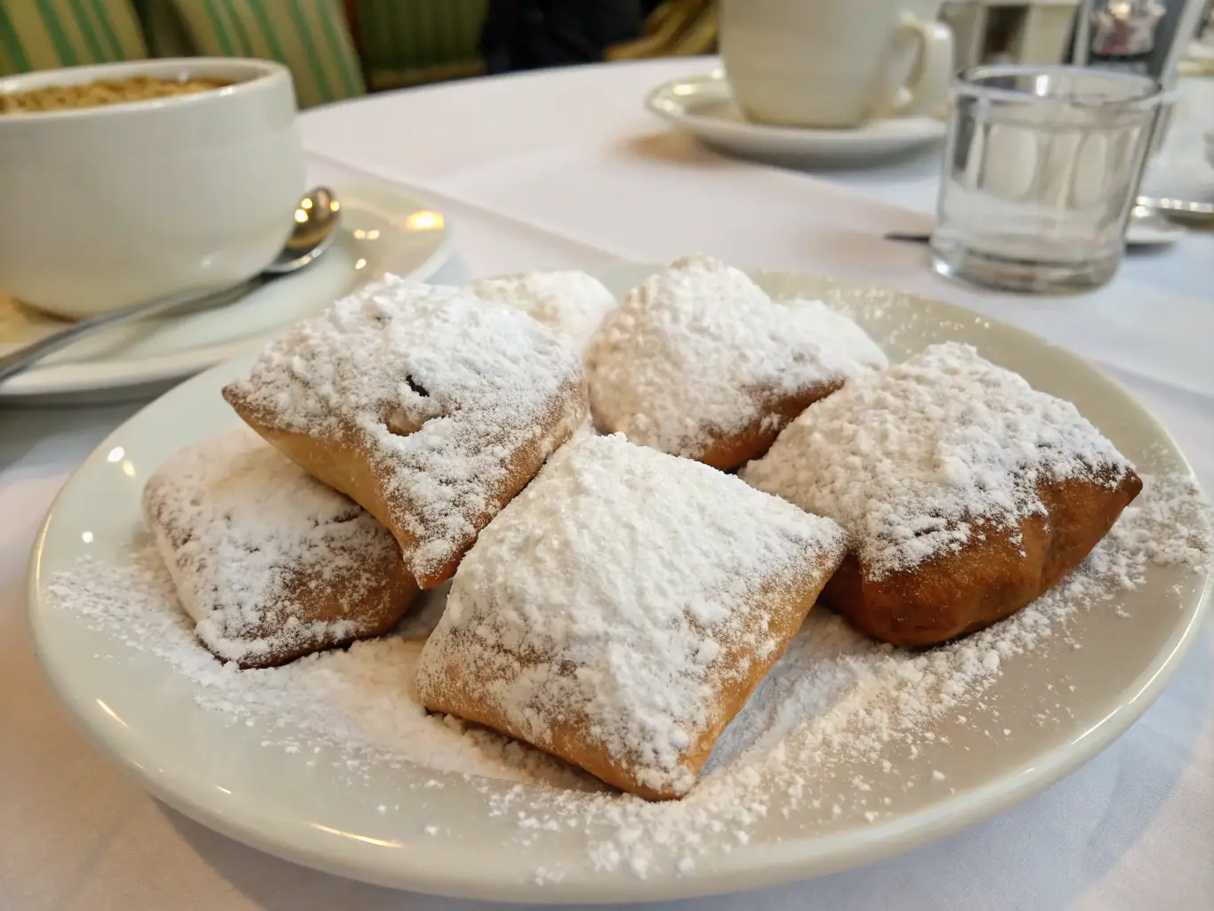 A tempting shot of golden, sugar-dusted beignets stacked on a plate, with a drizzle of chocolate sauce and a sprig of mint, set against a warm, inviting background.